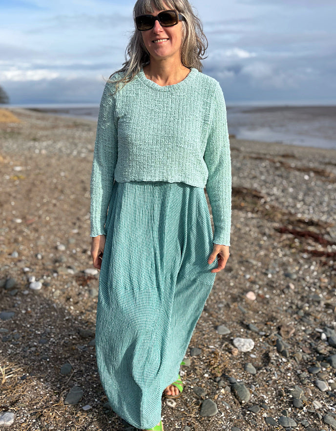 Woman in a teal outfit standing on a beach with ocean in the background