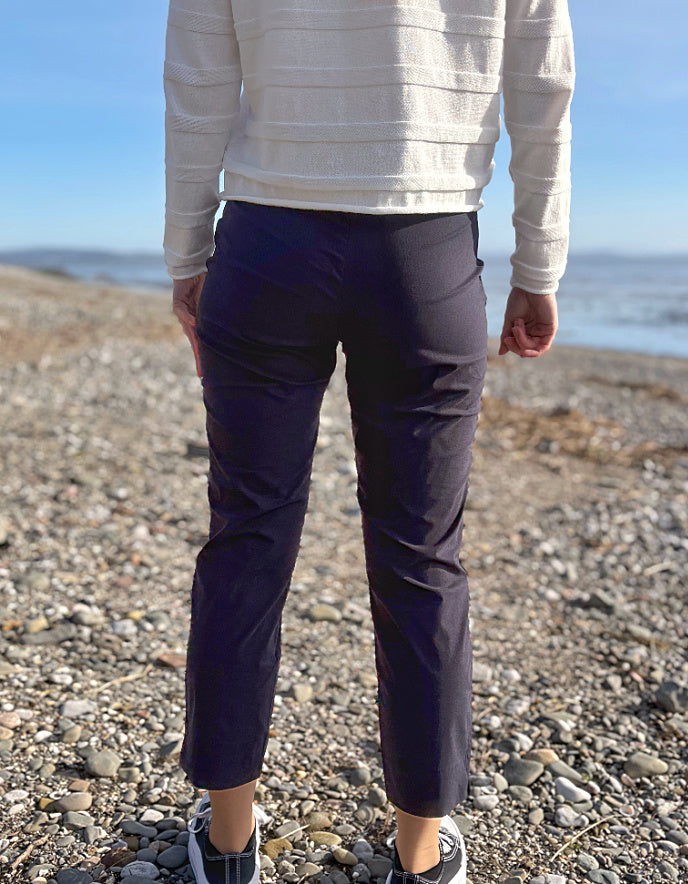 Person wearing black pants and white sneakers on a pebbly beach with ocean in the background