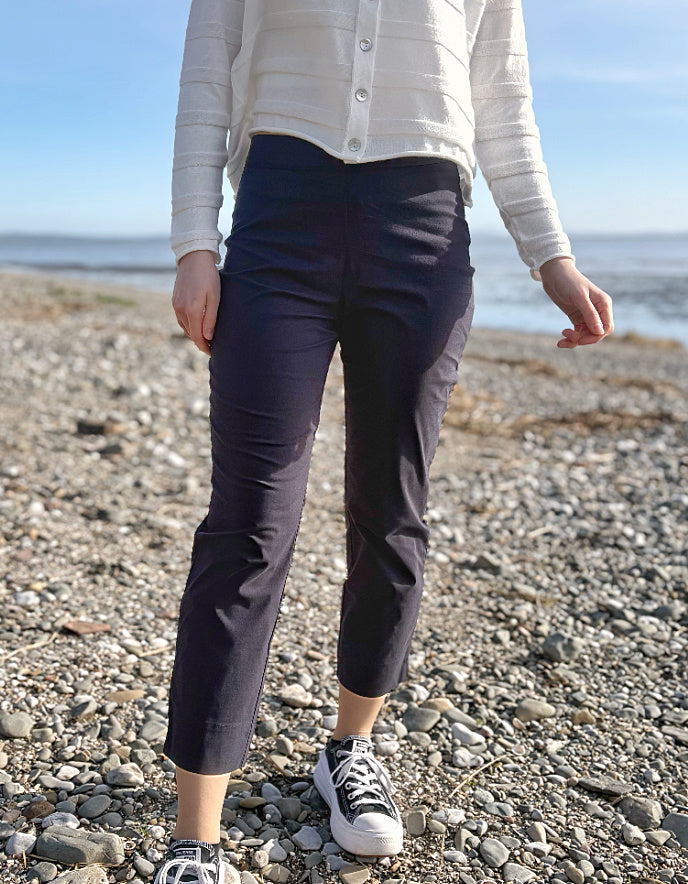 Person wearing navy pants and a light-colored sweater on a pebbly beach.