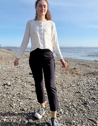 Person standing on a pebbly beach wearing a white shirt and black pants.