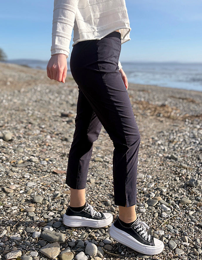Person wearing black pants and sneakers on a pebbly beach with ocean view