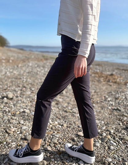 Person wearing black pants and white sneakers on a pebbly beach with ocean in the background