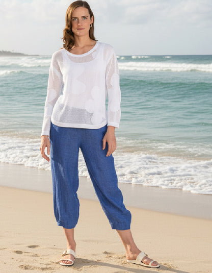 Woman standing on a beach wearing a white top and blue pants.