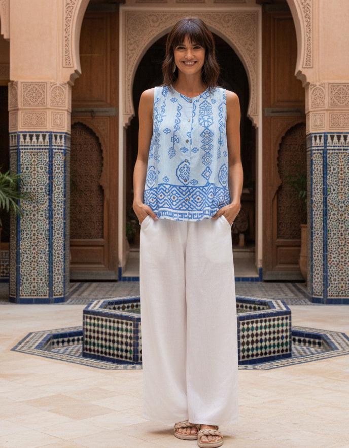 Woman wearing a blue patterned top and white pants standing in a decorative courtyard.