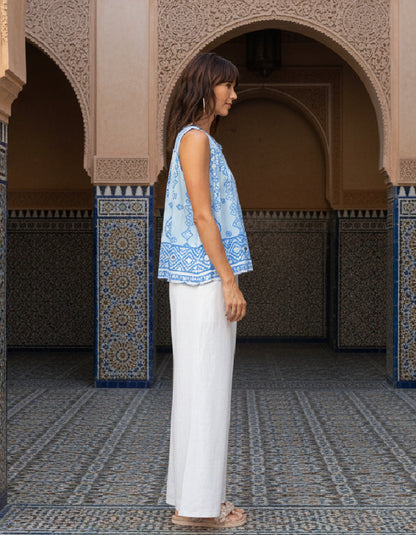 Woman in a blue patterned top and white pants standing in front of ornate arches with decorative tiles.