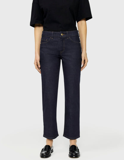 A model wearing dark navy blue cropped jeans with a straight-leg fit, paired with a black t-shirt and black leather loafers, shot against a light gray studio background.