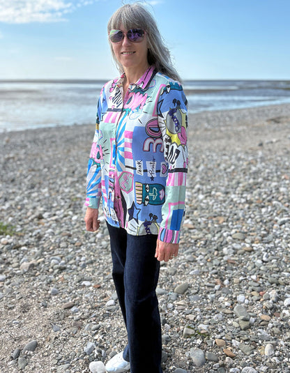 Woman wearing a colorful patterned shirt on a pebbly beach.