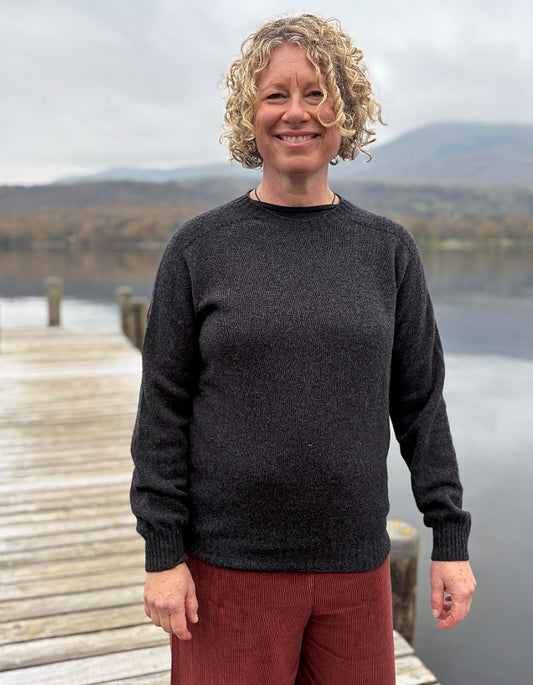 Woman wearing a dark sweater and red pants standing on a dock with a lake and mountains in the background