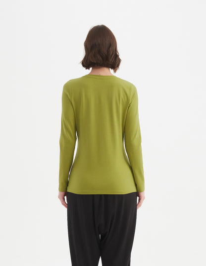 Person wearing a green long-sleeve top and black pants on a white background
