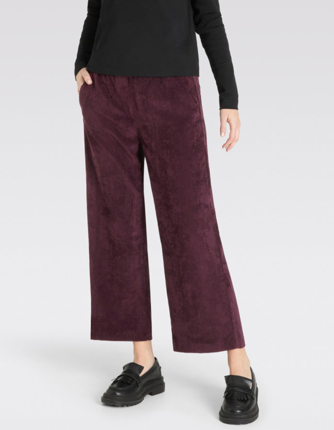 Person wearing burgundy corduroy pants with a black top on a white background