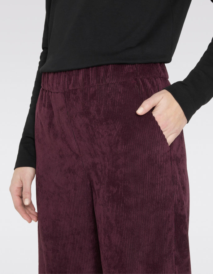 Maroon corduroy pants worn with a black top on a white background