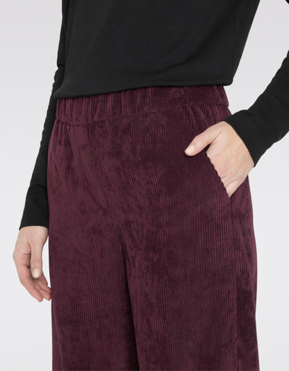 Maroon corduroy pants worn with a black top on a white background