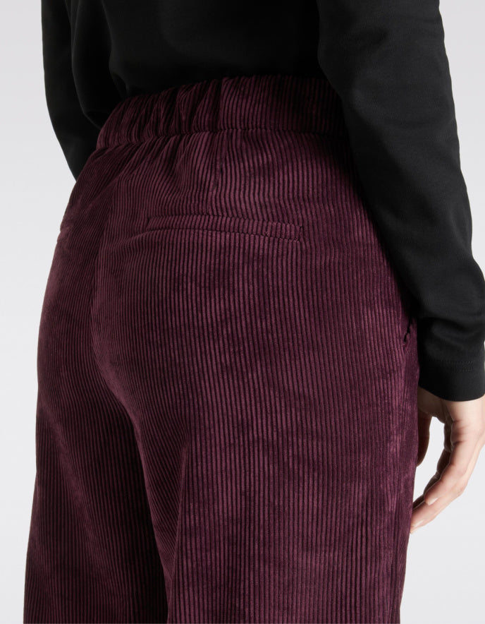 Maroon corduroy pants worn by a person on a white background
