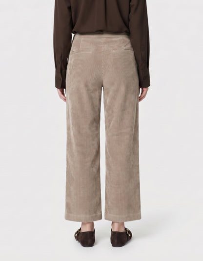 A person wearing wide-leg cropped trousers in a taupe corduroy fabric, paired with white sneakers and a white top, shown from the waist down on a light grey studio background.