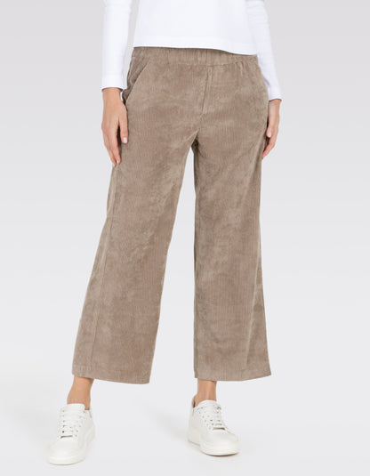 A model wearing a pair of wide-leg cropped pants in a light taupe corduroy fabric, styled with a white long-sleeve top and white sneakers against a light gray studio background.