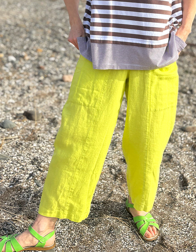 Person wearing bright yellow pants and green sandals on a beach.