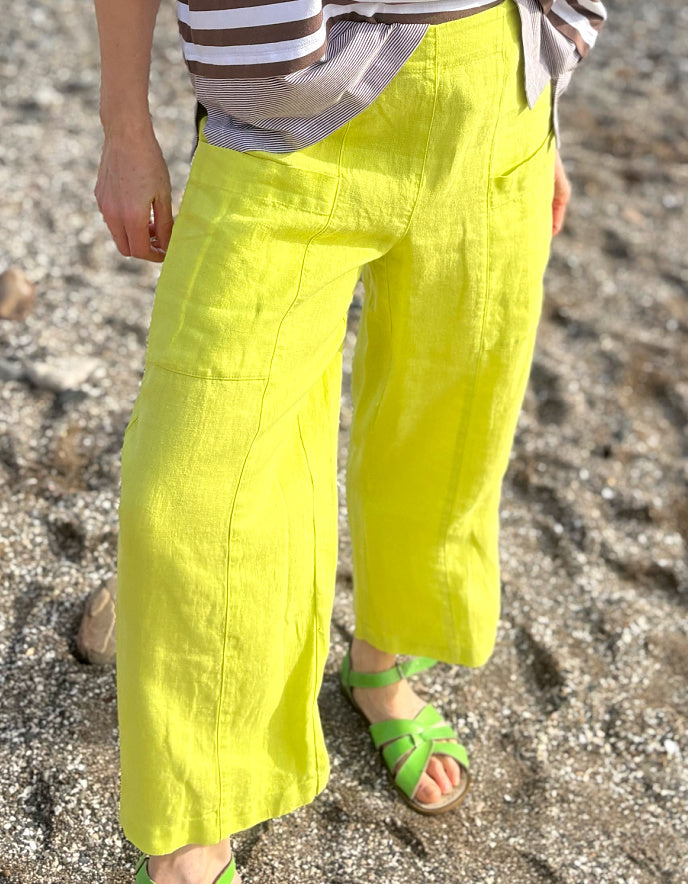 Person wearing bright yellow pants and green sandals on a sandy surface