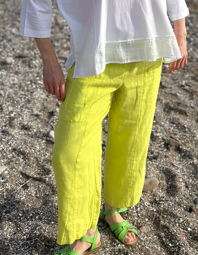 Person wearing bright yellow pants and green sandals on a beach.