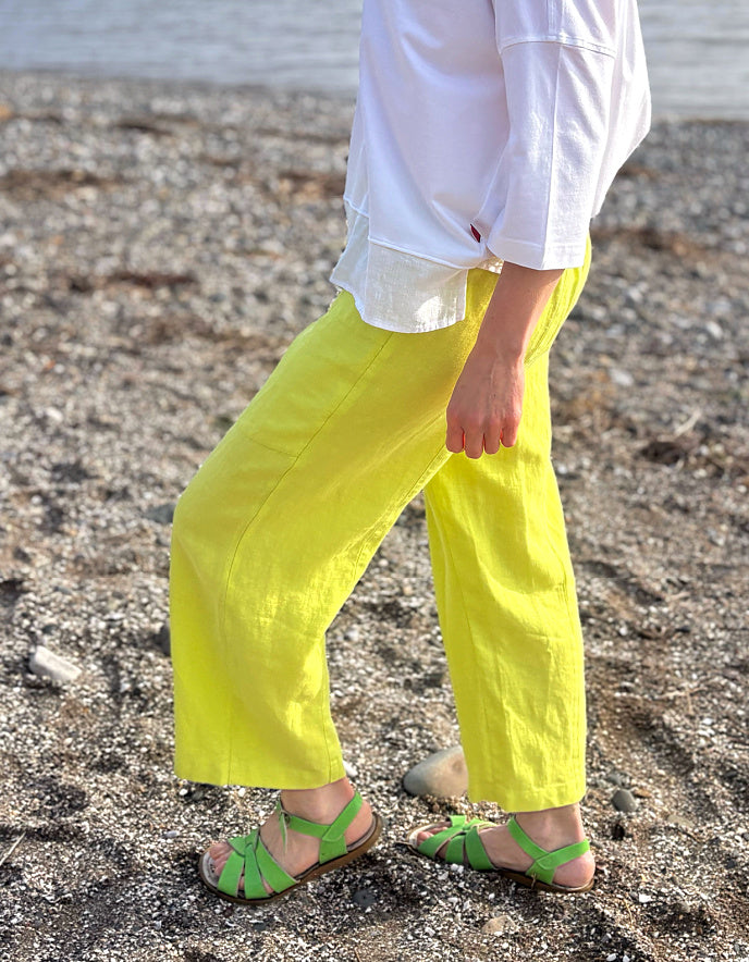 Person wearing bright yellow pants and green sandals on a beach.