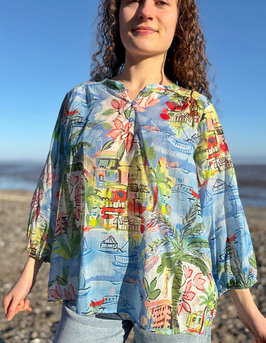 Woman wearing a colourful coastal print cotton shirt with a beach-themed design on a beach.
