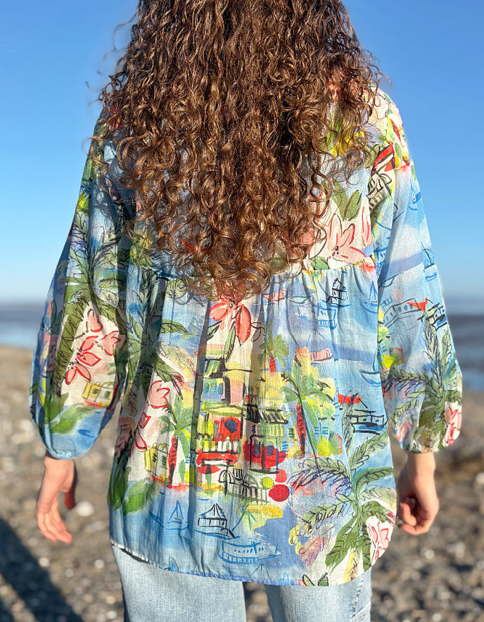 Woman wearing a colourful coastal print cotton shirt with a beach-themed design on a beach.