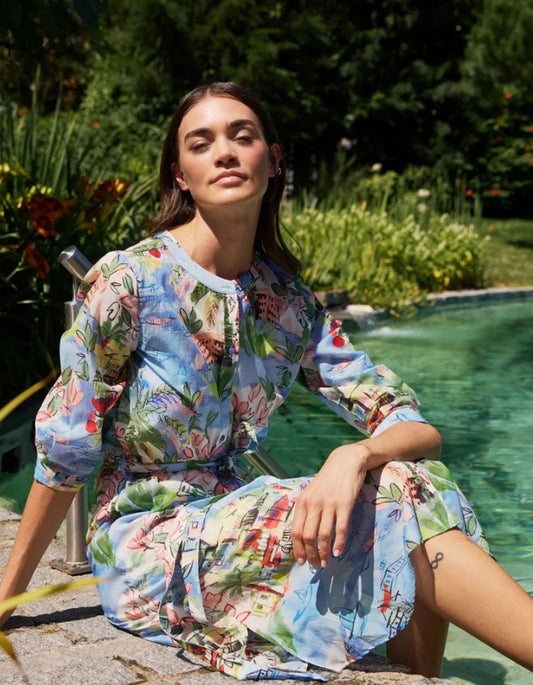 Woman in a colorful floral dress sitting by a pool with greenery in the background