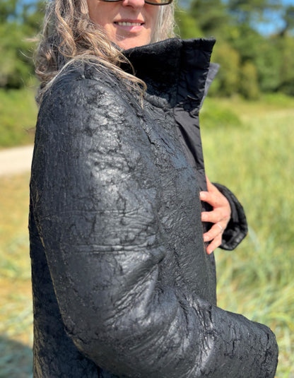 Person wearing a black textured jacket outdoors with greenery in the background