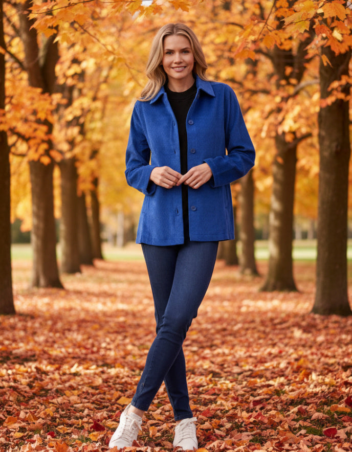 Woman in a blue coat standing in an autumn park with trees and fallen leaves.