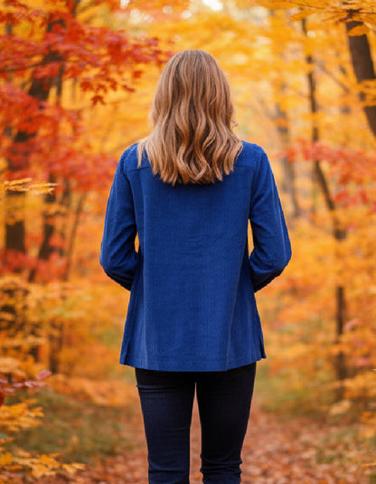 Person wearing a blue cord jacket standing in an autumn forest with orange and yellow leaves.