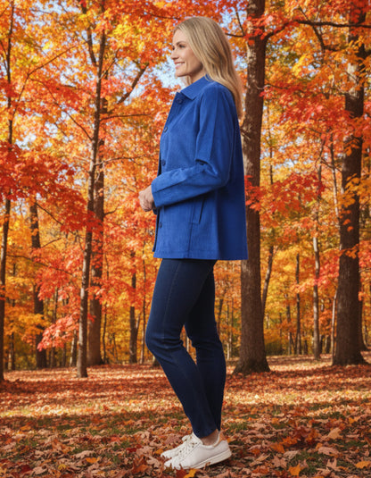 Woman in a blue cord jacket standing in an autumn forest with colourful trees.