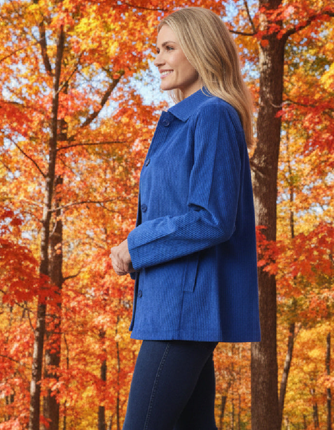 Woman in a blue cord jacket standing in an autumn forest with colourful trees.
