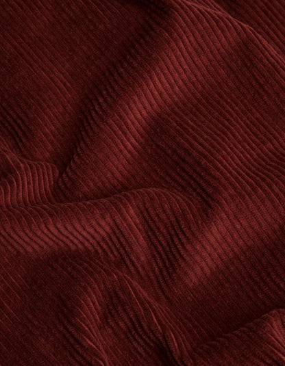 A close-up of draped corduroy fabric in a deep burgundy red color, showing the ribbed texture and soft folds.