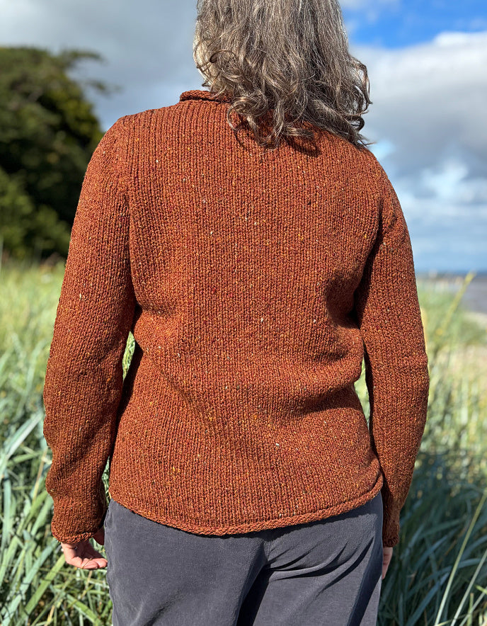 Woman wearing a coper brown donegal tweed sweater standing in a field with a scenic background