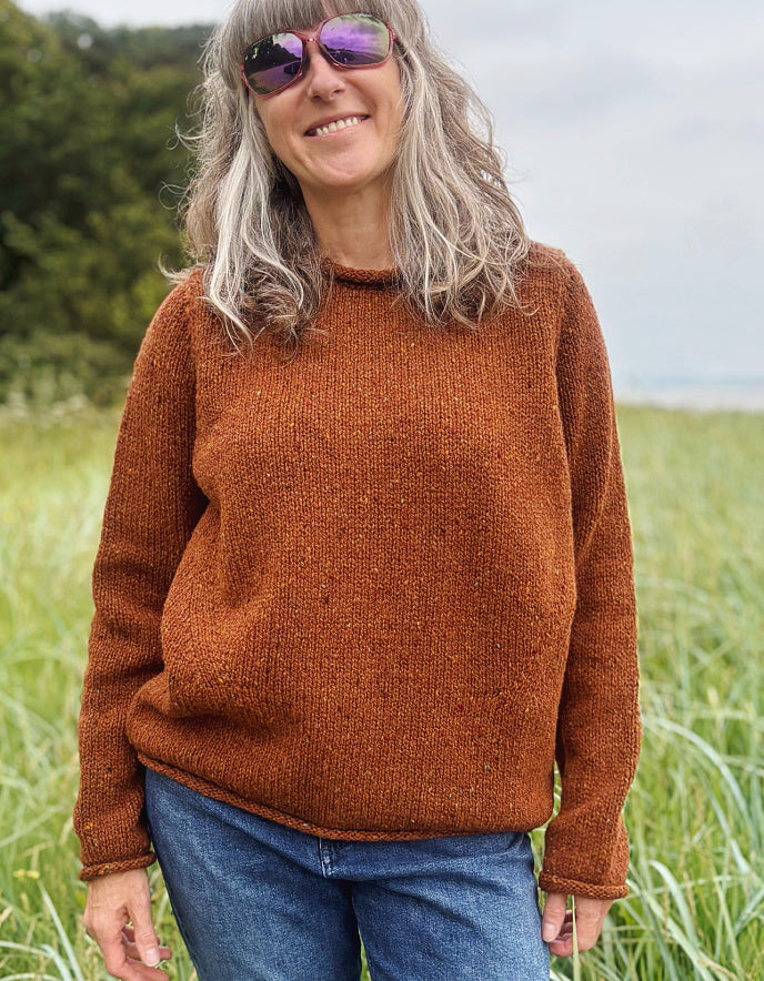 Woman wearing a coper brown donegal tweed sweater standing in a field with a scenic background