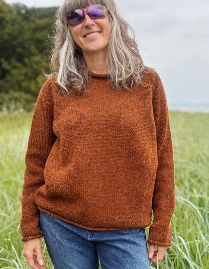 Woman wearing a coper brown donegal tweed sweater standing in a field with a scenic background
