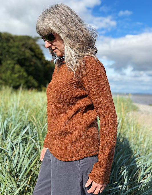 Woman wearing a coper brown donegal tweed sweater standing in a field with a scenic background