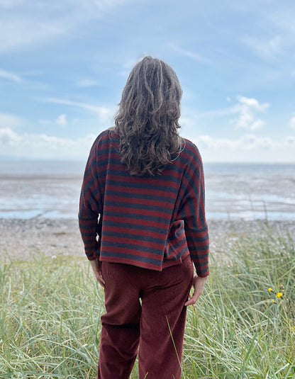 Person wearing a copper and charcoal striped turtle neck sweater with copper corduroy wide leg trousers and sunglasses on a beach