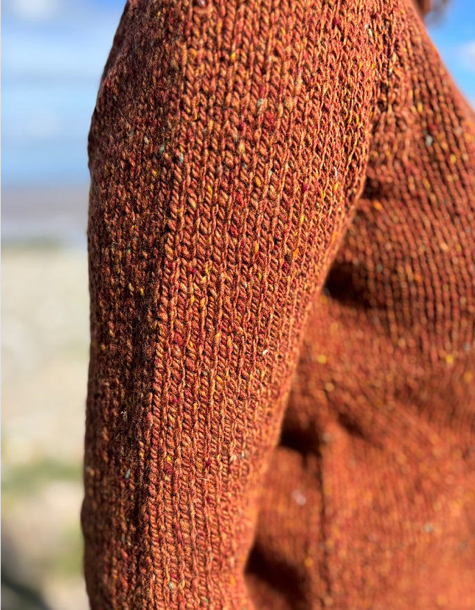 Woman wearing a coper brown donegal tweed sweater standing in a field with a scenic background