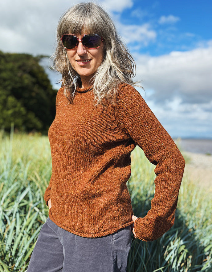 Woman wearing a coper brown donegal tweed sweater standing in a field with a scenic background