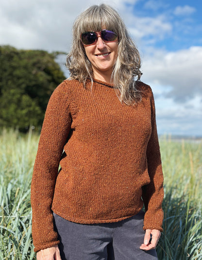 Woman wearing a coper brown donegal tweed sweater standing in a field with a scenic background