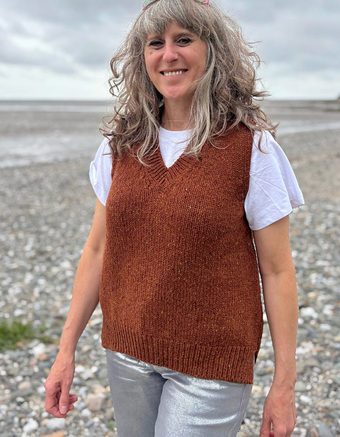 Woman wearing a brown donegal tweed knitted vest over a white shirt in a grassy field.