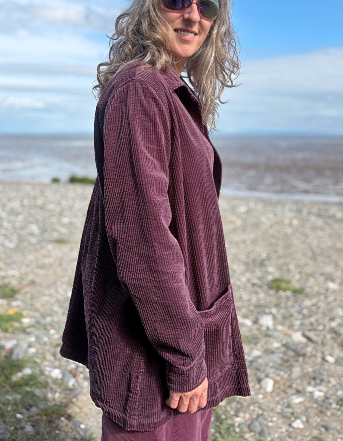 Woman standing on a beach wearing a purple jumbo corduroy blazer and pink shirt.