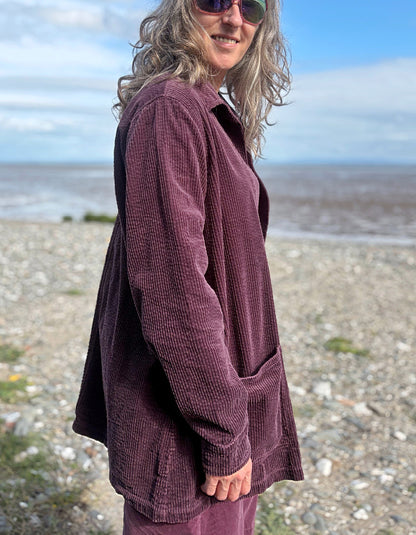 Woman standing on a beach wearing a purple jumbo corduroy blazer and pink shirt.