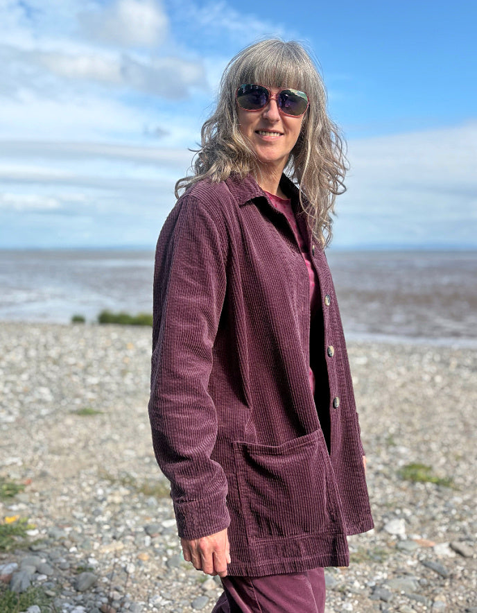 Woman standing on a beach wearing a purple jumbo corduroy blazer and pink shirt.
