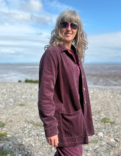 Woman standing on a beach wearing a purple jumbo corduroy blazer and pink shirt.