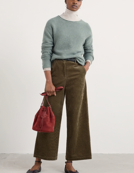 Person wearing a green sweater and brown pants holding a red bag on a white background