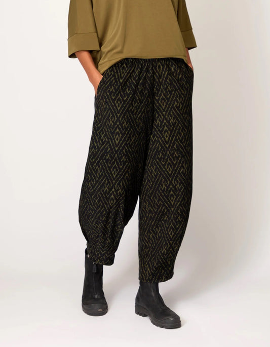 Person wearing black patterned pants and a green top on a white background
