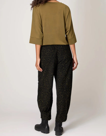 Person wearing an olive green top and black patterned pants on a white background