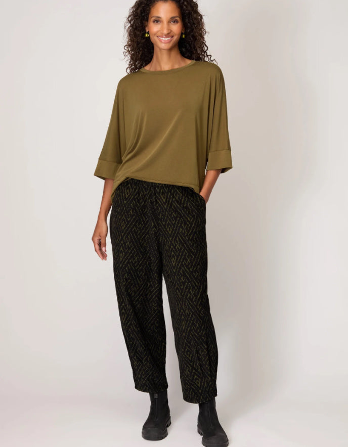 Woman wearing an olive green top and black patterned pants on a white background