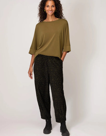 Woman wearing an olive green top and black patterned pants on a white background